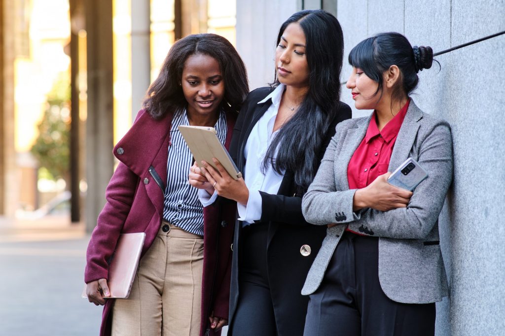Elegant diverse female coworkers sharing tablet on street
